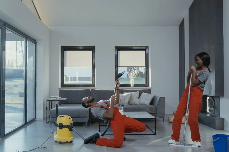 Individual in protective gear cleaning microwave using spray bottle and cloth indoors.