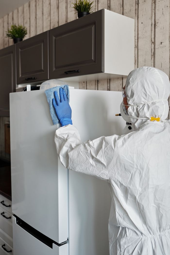 who-we-are Healthcare worker in protective gear disinfects a refrigerator to ensure safety and cleanliness.